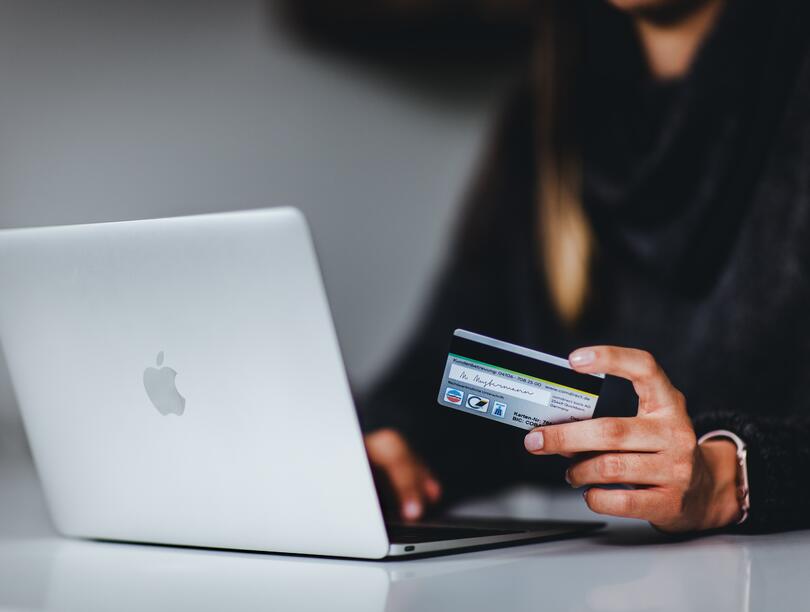 Person holding credit in one hand, while the other hand is typing on a laptop