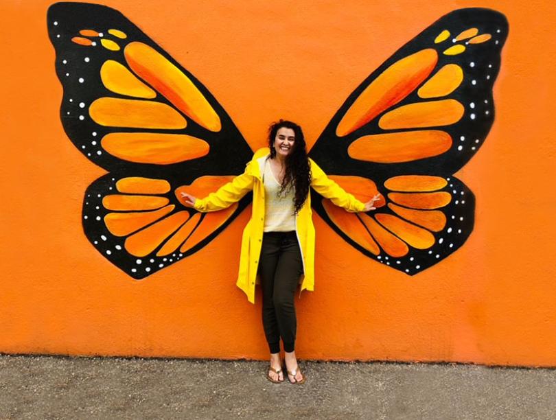 Dr. Sana Shahram standing in front of an orange butterfly mural wall.