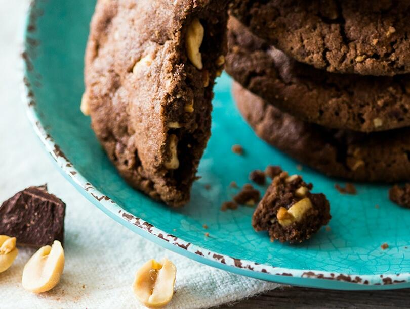 Stack of chocolate cookies on a plate, with peanuts and crumbs beside it