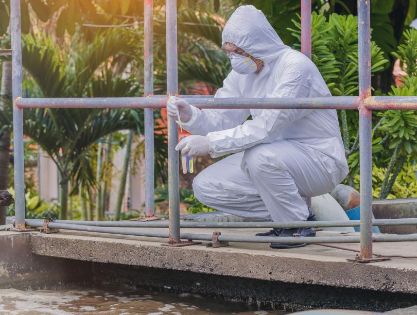 Scientist in protective body suit tests wastewater at outdoor treatment facility