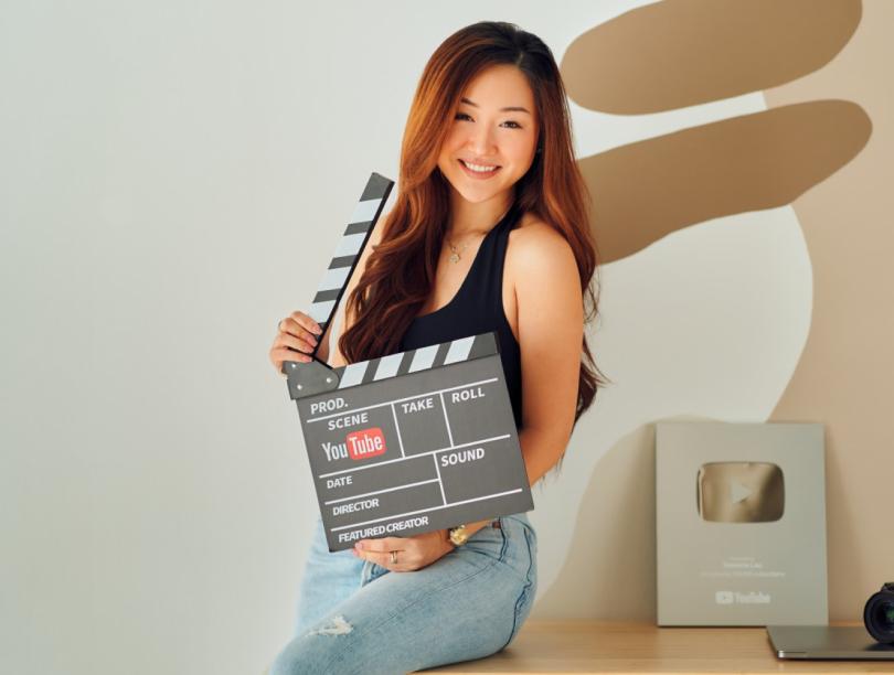 Asian woman leaning against desk and holding open a film clapboard