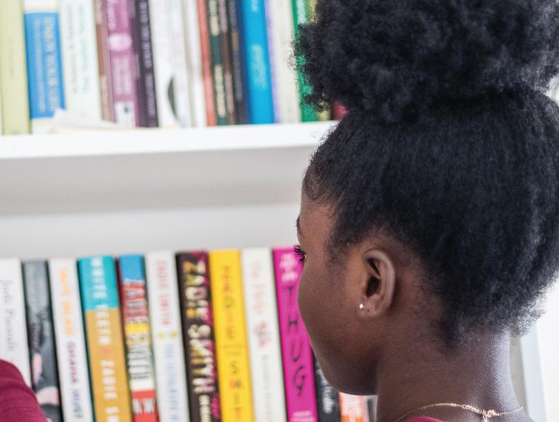 Black girl browsing through books on shelves