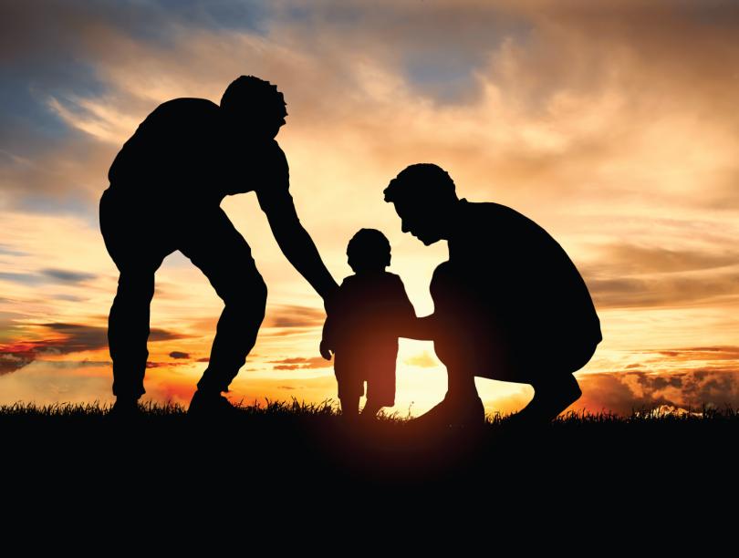 Silhouettes of two men with toddler in front of sunrise