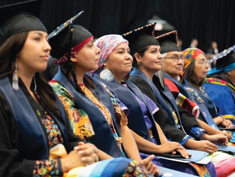 Indigenous grads in cap and gowns seated at graduation ceremony
