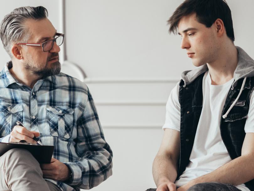 Male therapist with clipboard listening to young man