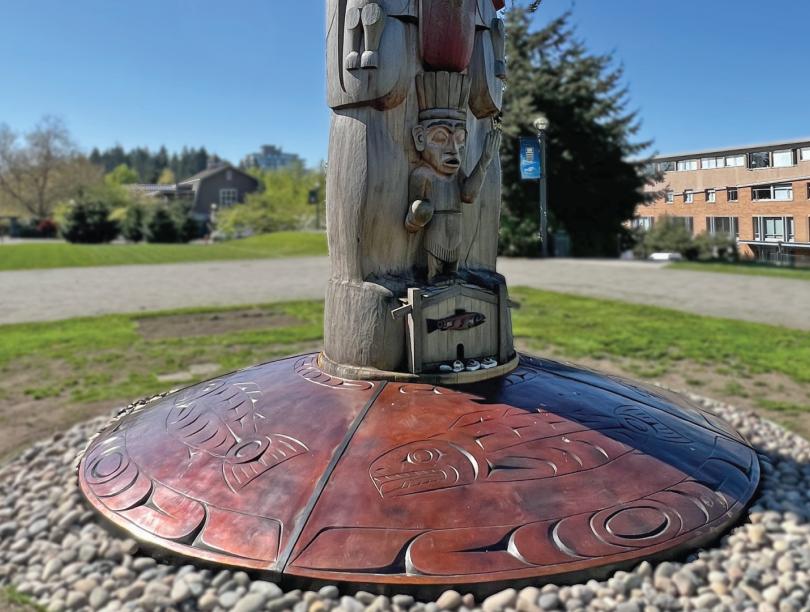 Indigenous bronze artwork at the base of a totem pole