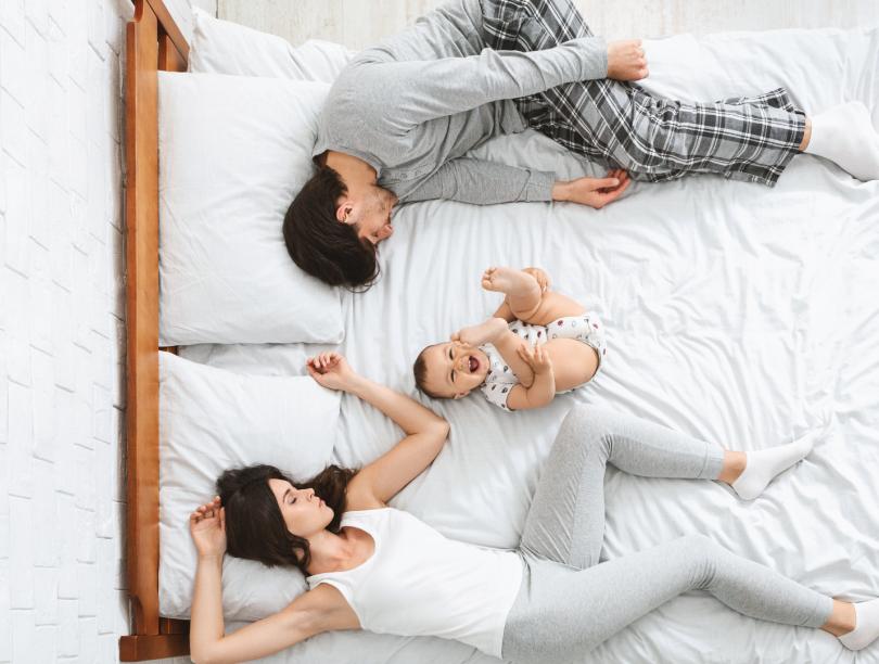 Aerial shot of parents lying on bed with baby between them
