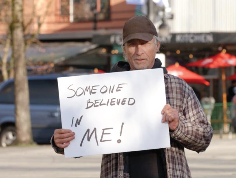 Man stands on street with sign stating "Someone believed in me!"