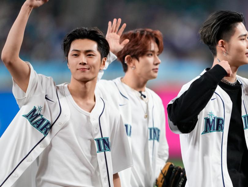 Three Asian young men in baseball jerseys wave at crowd