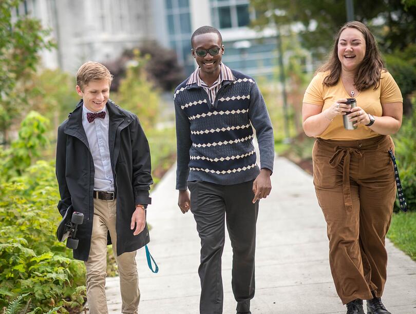 Three colleagues smiling and walking outdoors with greenery on the left