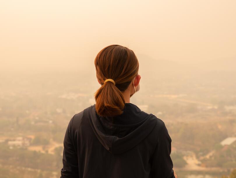Woman sitting facing city shrouded in haze