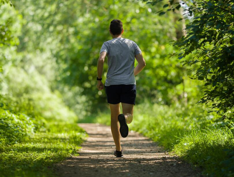 Man in shorts jogging along path in forest