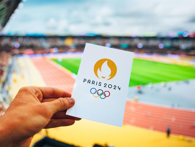 A card reading "Paris 2024" is held in front of a running track