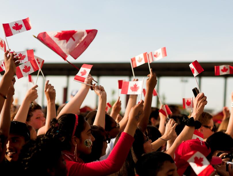 A crowd of people wave Canadian flags