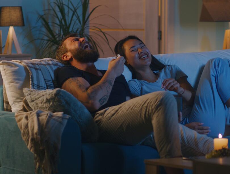 Man and woman laughing on couch in front of TV screen