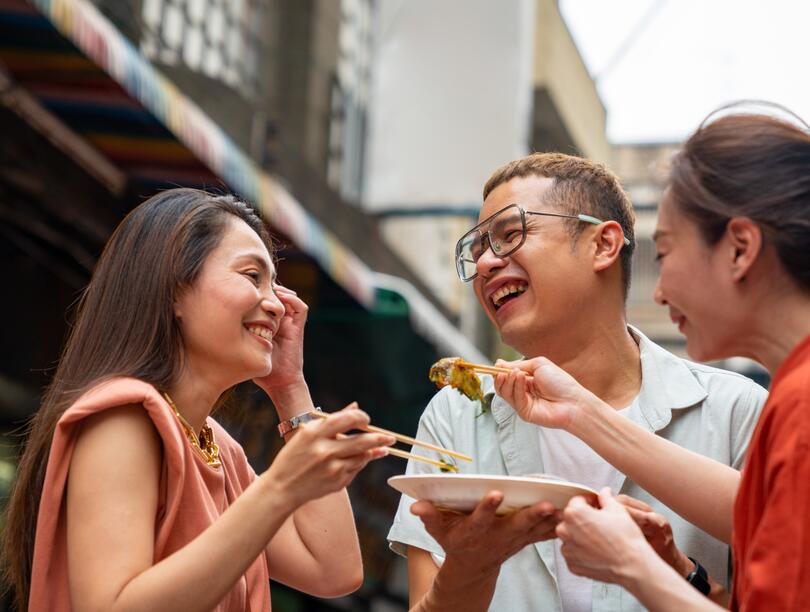 Two women and man eating from a plate with chopsticks