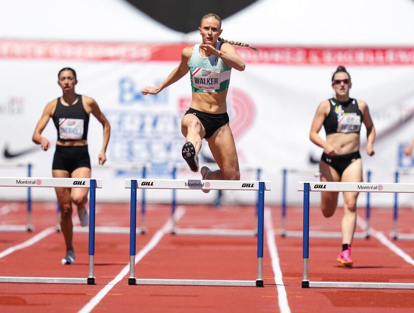 Five track-and-field athletes sprinting down a track with hurdles in each lane