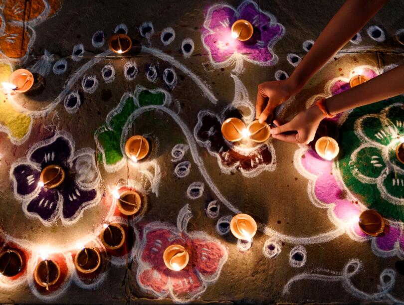 Overhead shot of colourful rangoli and lighted diyas