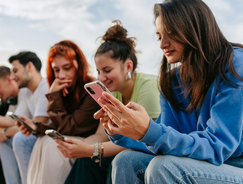 Young people sitting in a row outside looking at smartphones