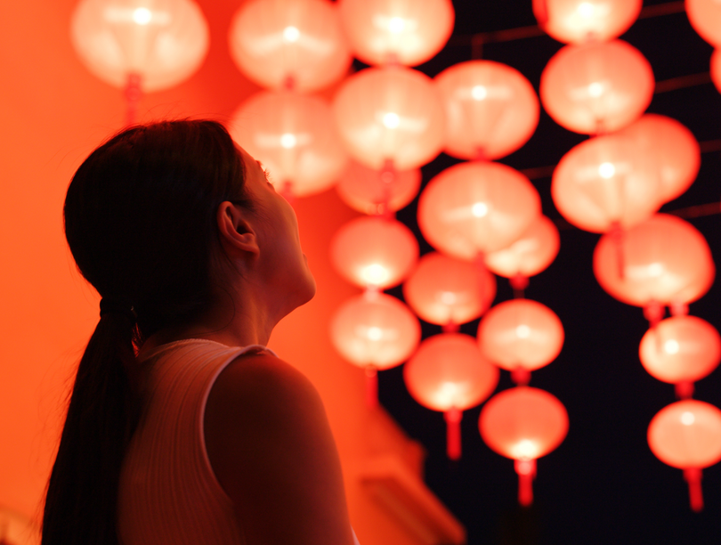 Side profile of a woman staring up at red lanterns that are glowing against the black sky