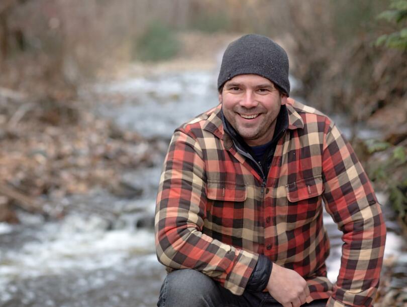 Dr. Adam Ford outdoors, with a creek behind him
