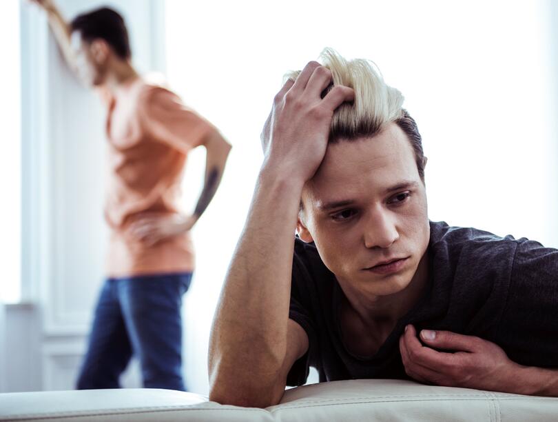 Stressed-out guy on couch looks away from man staring out window