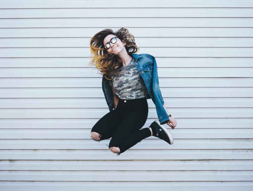 Woman in sunglasses jumping into air in front of wall