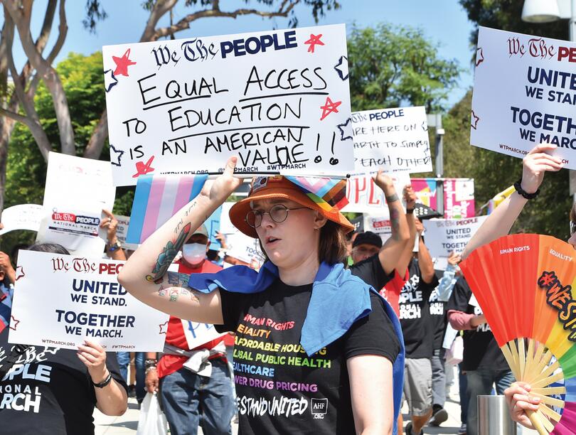 Protestors holding signs and displaying Pride rainbows