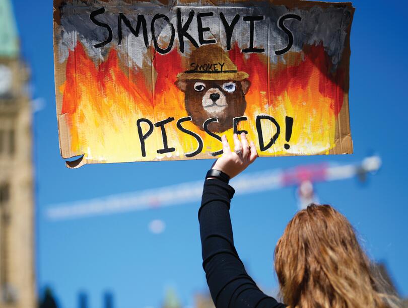 Woman holds wildfire protest sign at Canada's Parliament Hill