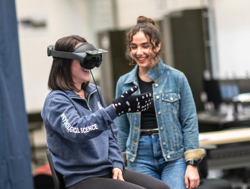 Woman wears VR headset and gloves as another woman watches 