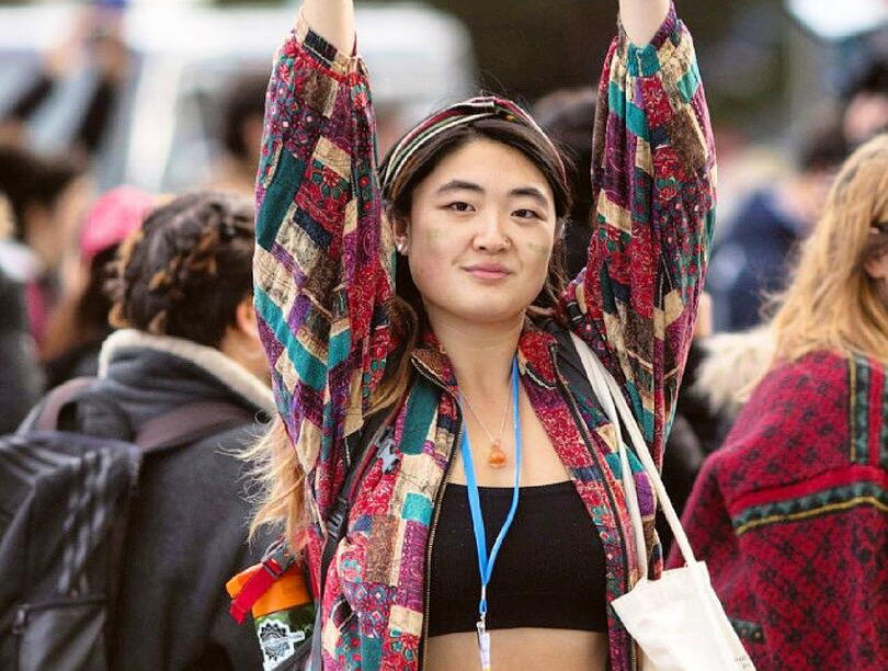 An image of Sophia Yang standing in front of a crowd with her arms up, wearing a lanyard, black top, and quilted red, green, and white top.