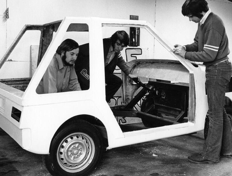 A black and white photo of three people working on the Wally Wagon