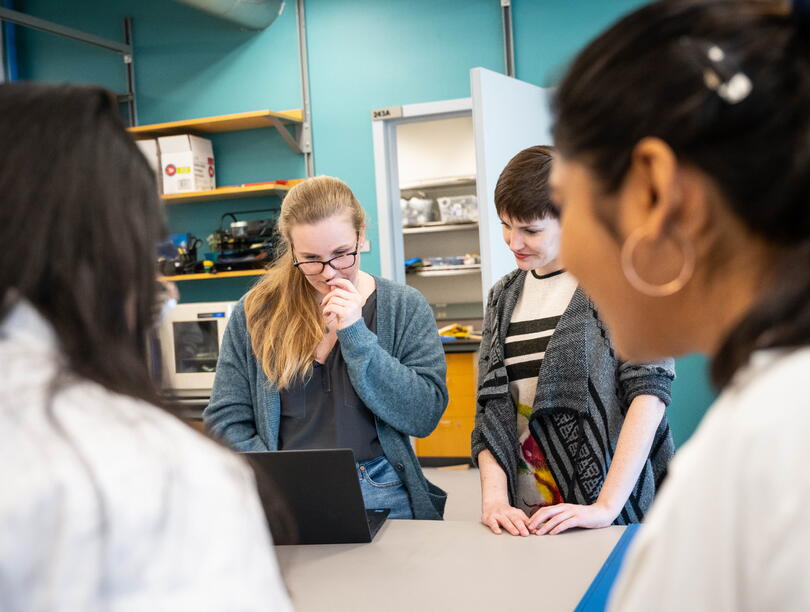 Three women gathered around fourth woman looking at laptop