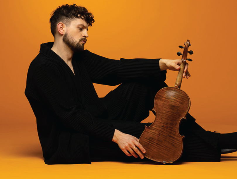 Man in black clothing sitting on ground with viola