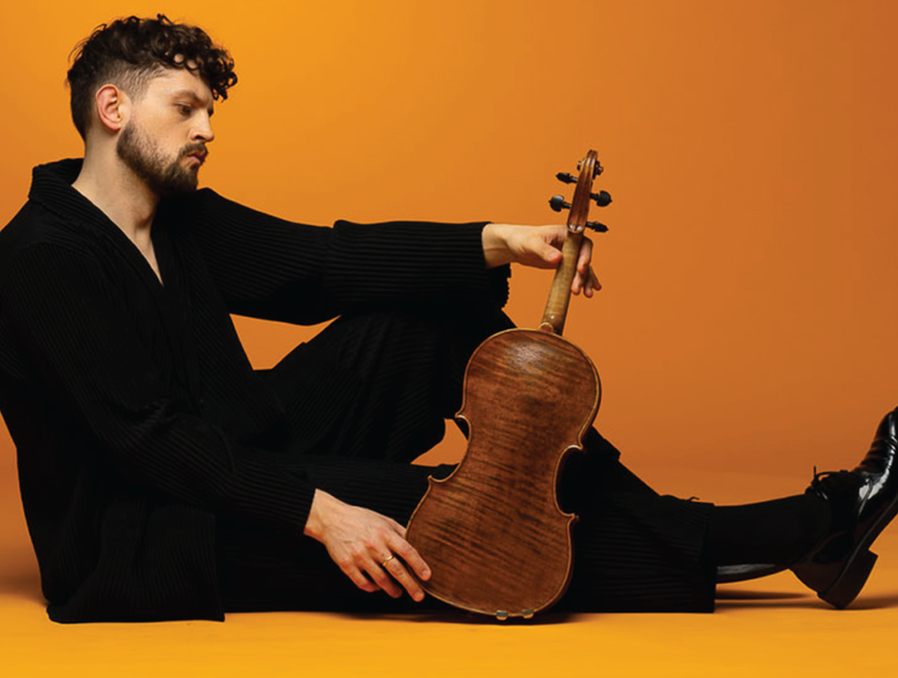 Man in black clothing sitting on ground with viola