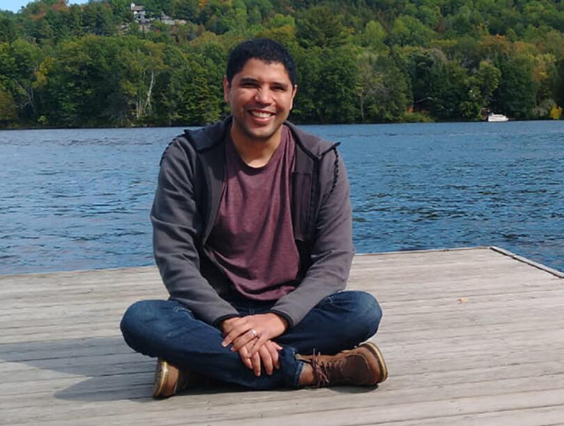 Hugo Mota Santos seated on a deck with water and trees in the background