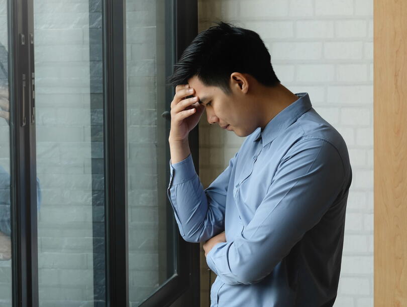 Man holds hand to forehead in front of windows