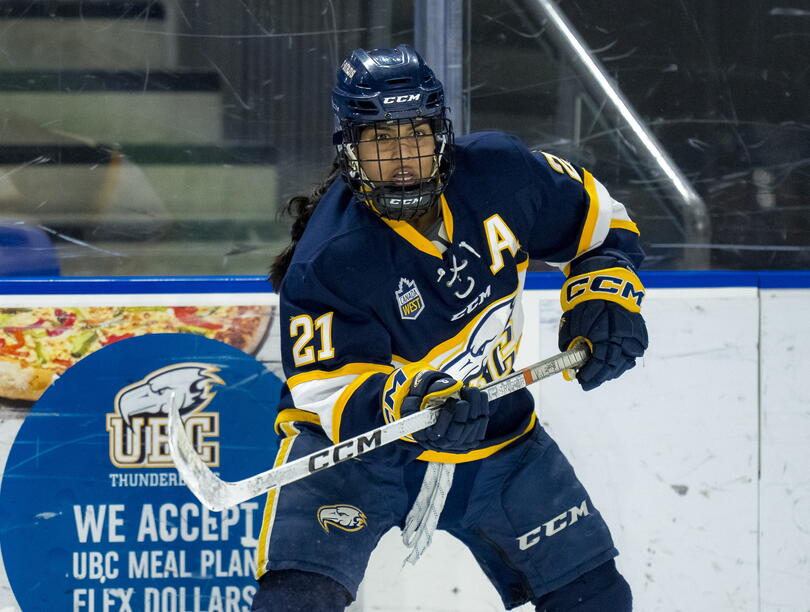 South Asian woman hockey player raises hockey stick on ice