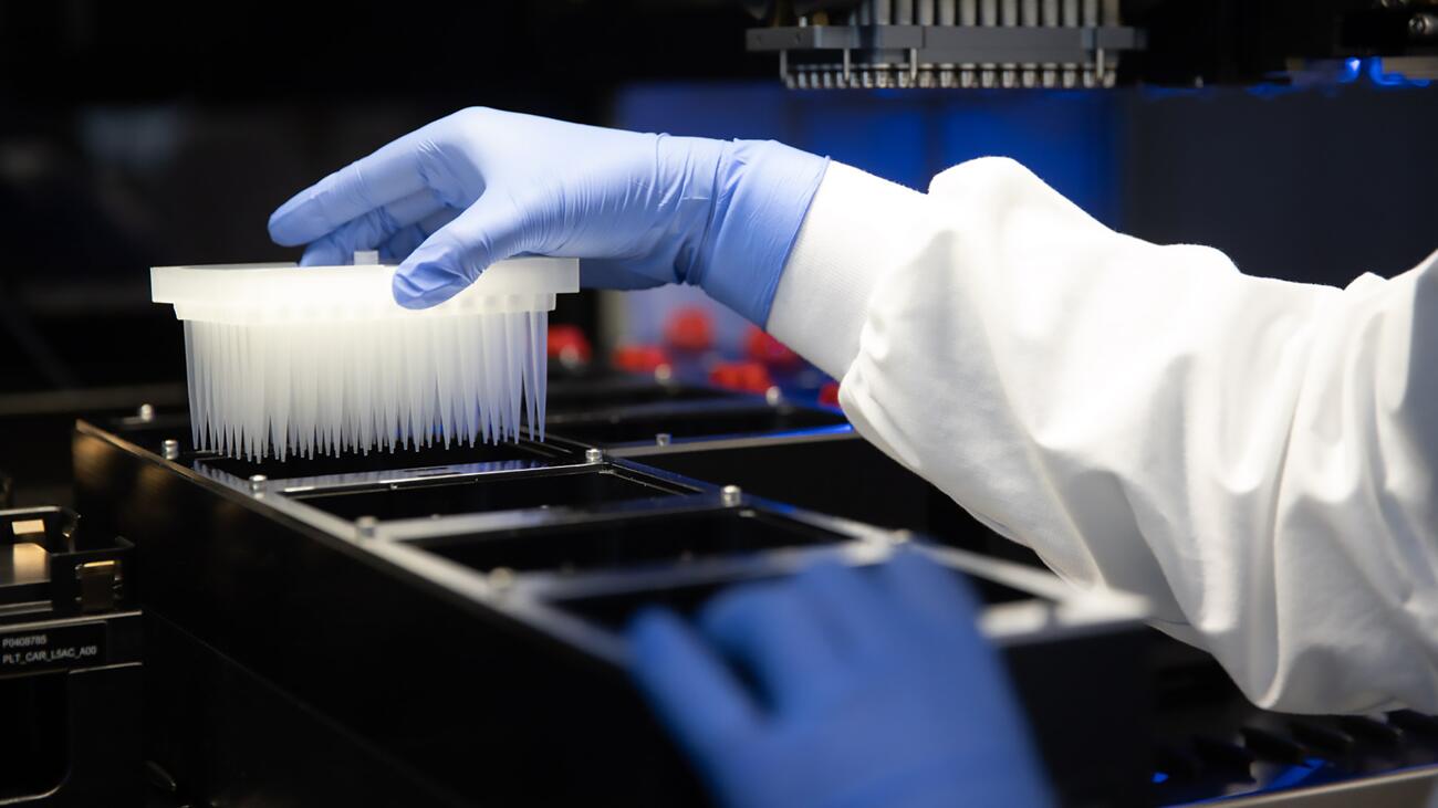 A lab worker loading a sample in white plastic containers onto a robotic arm