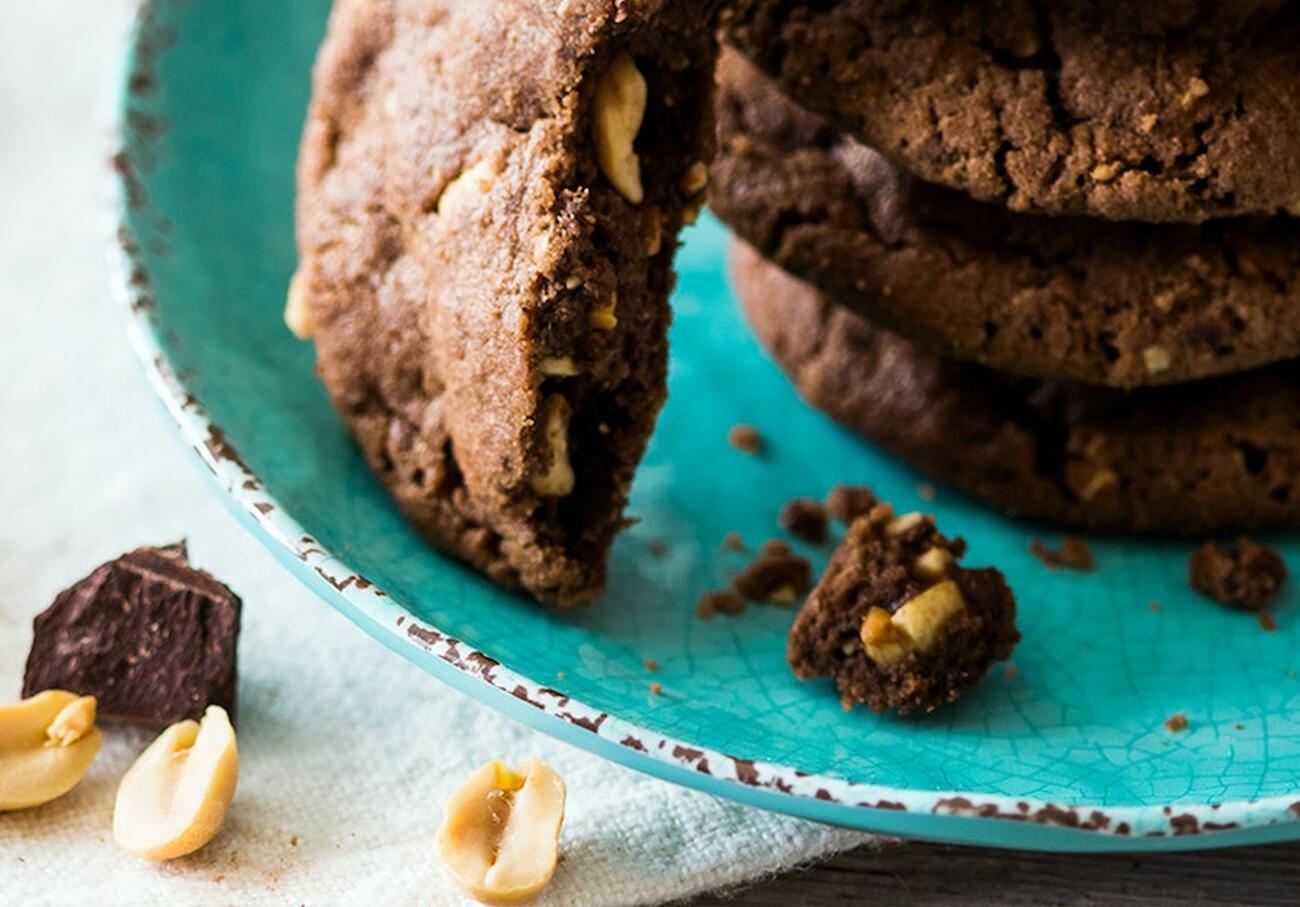 Stack of chocolate cookies on a plate, with peanuts and crumbs beside it