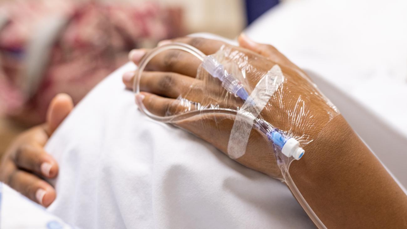 Patient in hospital with IV tube attached to hand holds pregnant stomach