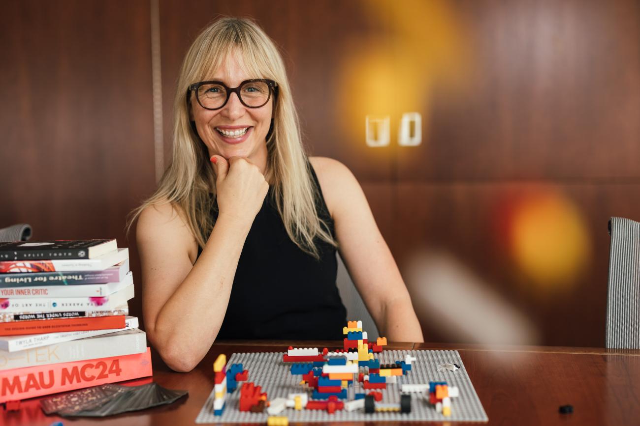 Dr. Kari Marken sits at a desk with lego, smiling at the camera.