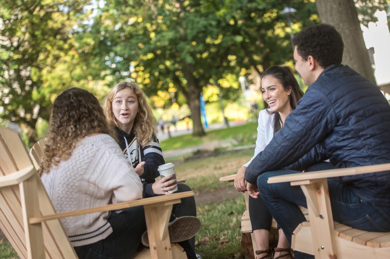 Four students sitting on chairs outside, with one student holding a coffee cup