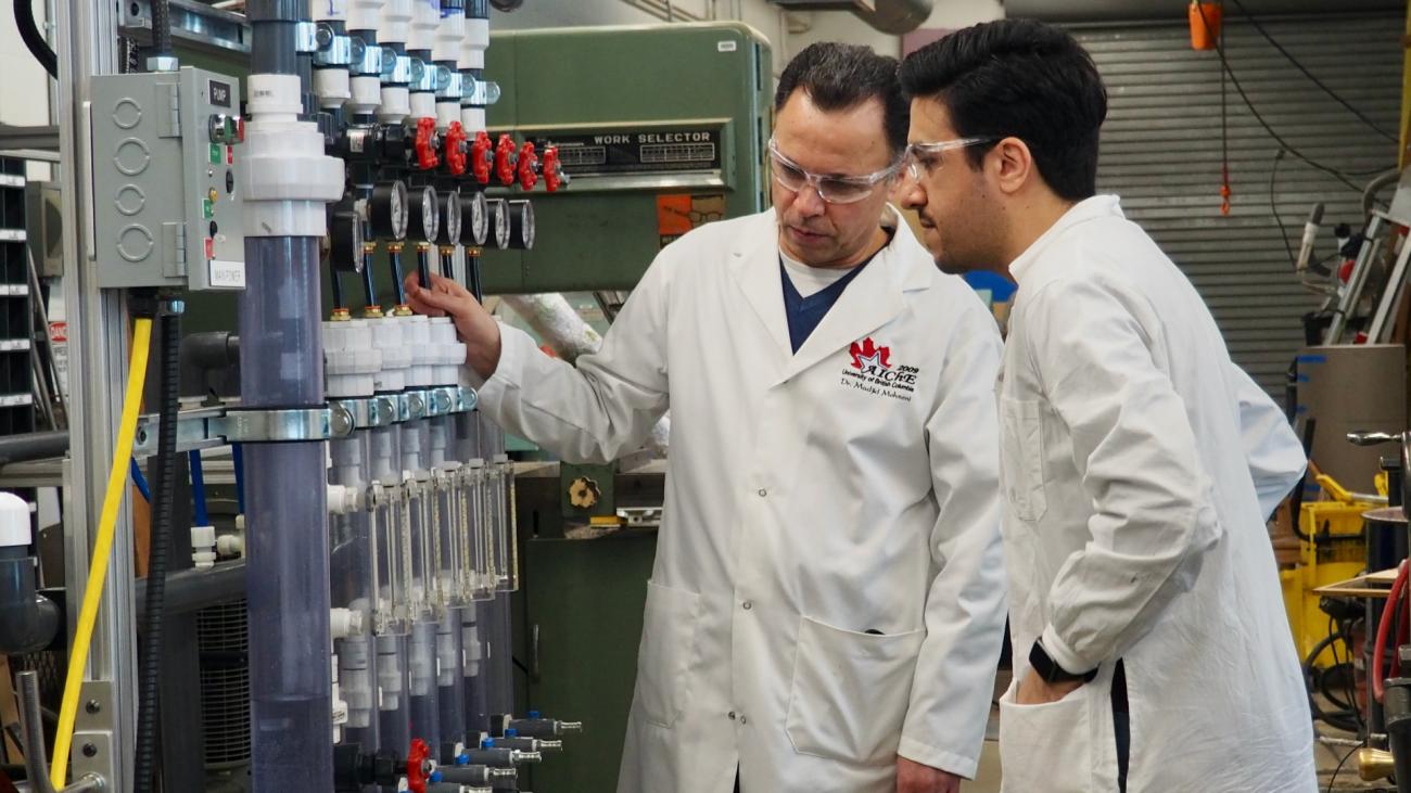 Two scientists in lab coats look at machine with large tubes