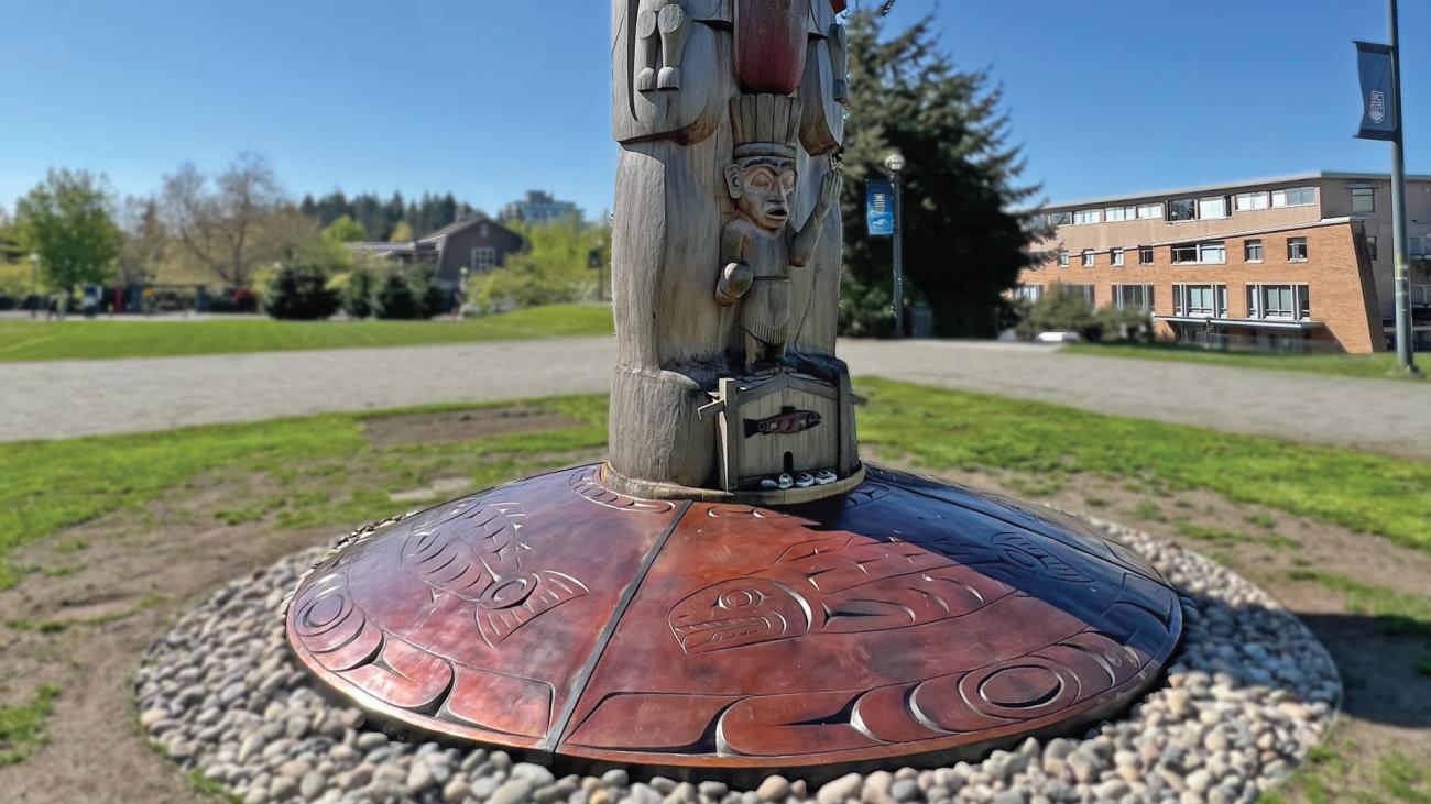 Indigenous bronze artwork at the base of a totem pole