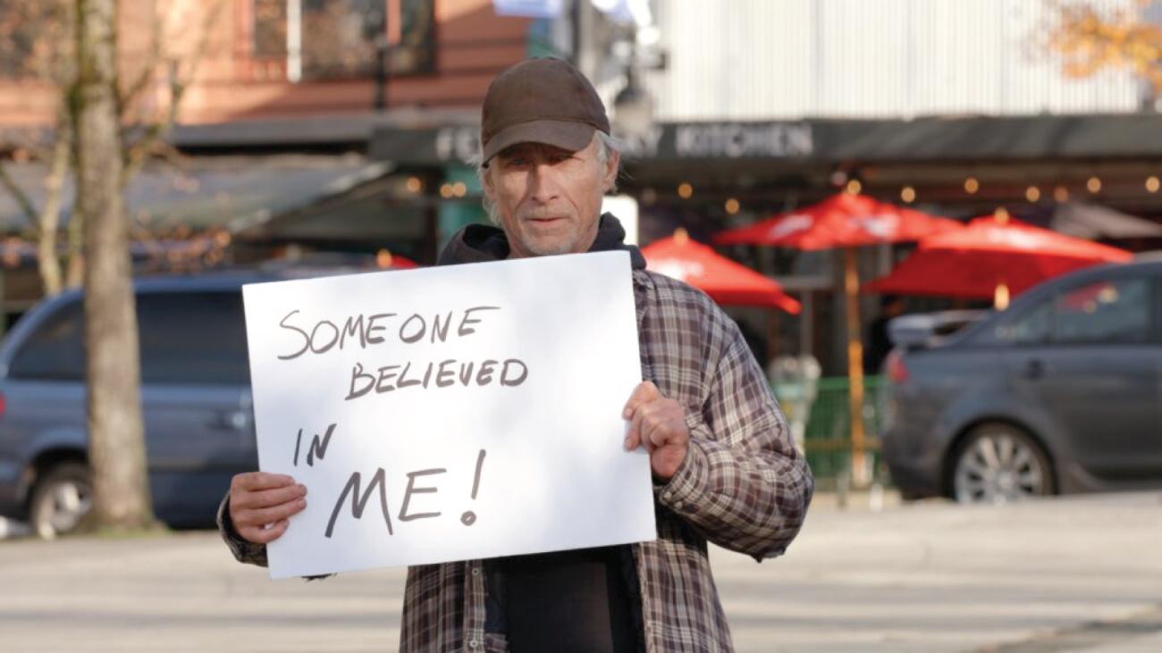 Man stands on street with sign stating "Someone believed in me!"
