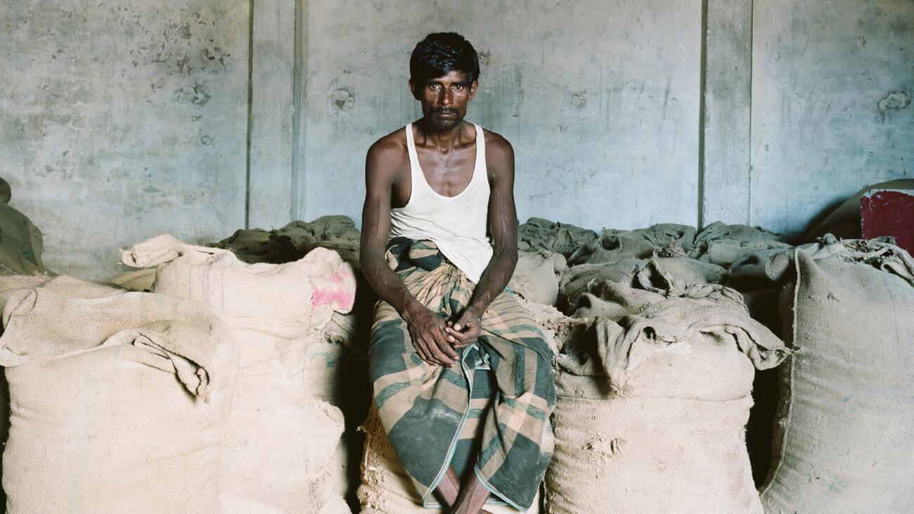 A person with short black hair and dark skin sits on a wall made of filled, upright sacks. 