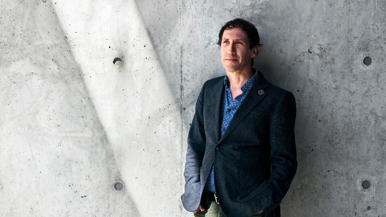 Kevin Leyton-Brown stands against a grey wall, wearing a dark blue suit.