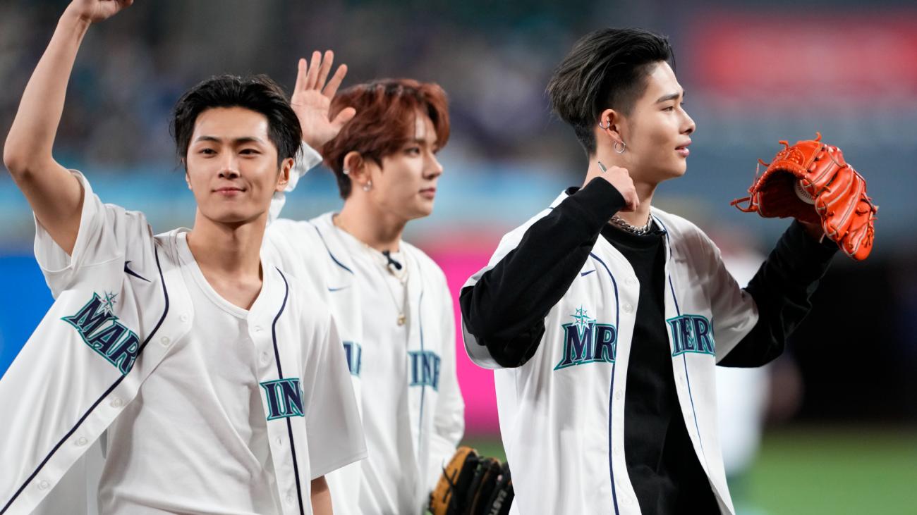 Three Asian young men in baseball jerseys wave at crowd