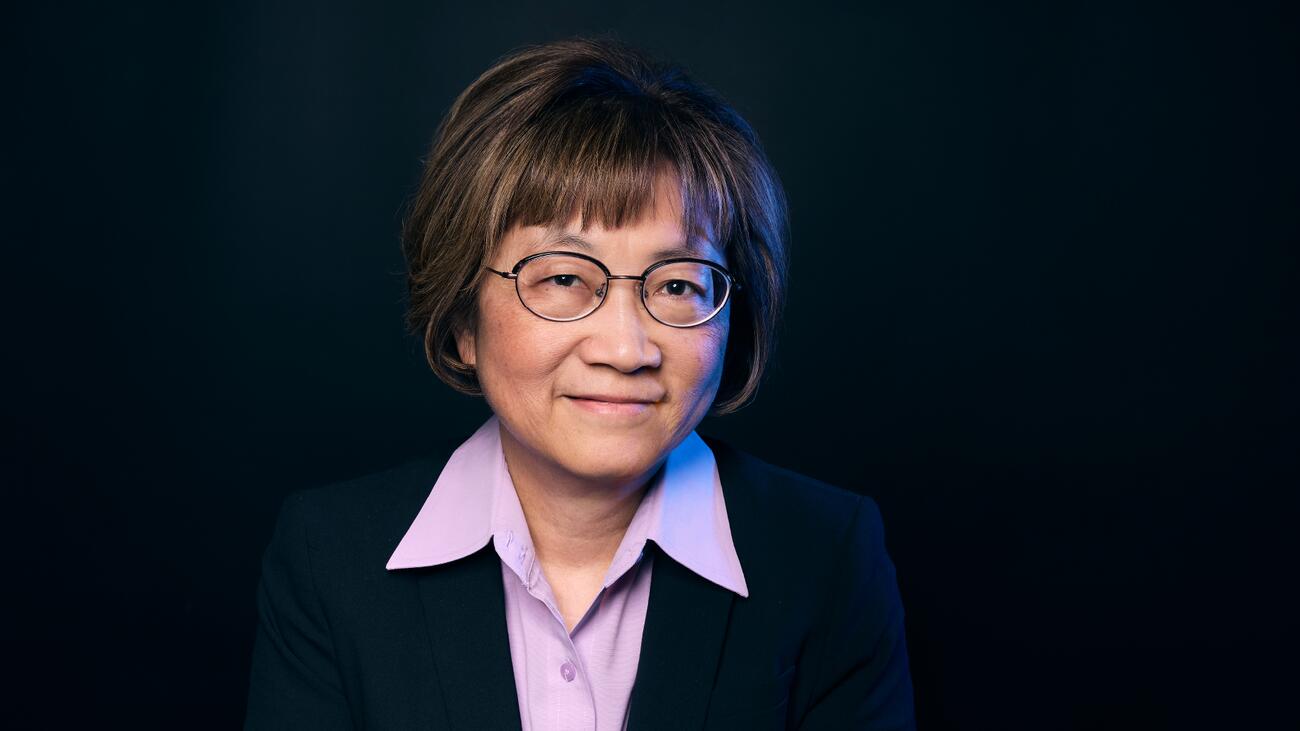 A headshot of Dr. Teresa Tsang with black glasses, short brown hair, and a purple collared shirt.